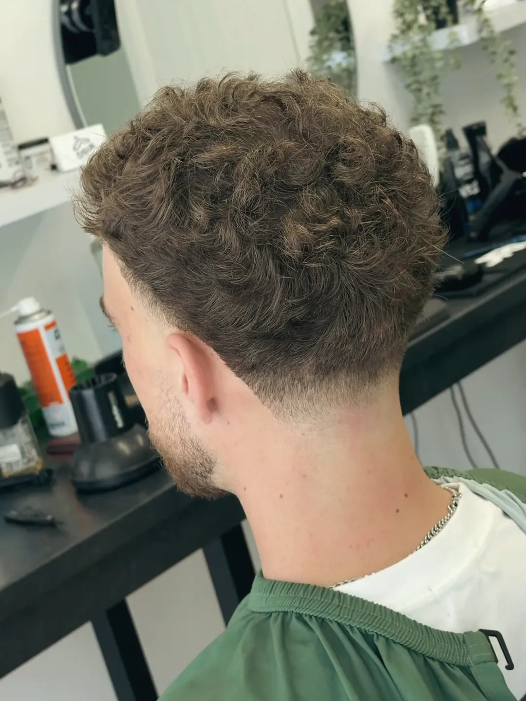 Back and side of a textured curly crop against a green cape.